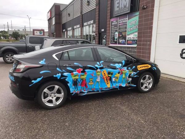 Une voiture noire avec une peinture colorée sur le côté est garée devant un immeuble.