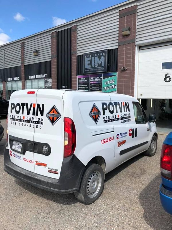 Une camionnette potvin blanche est garée devant un immeuble.