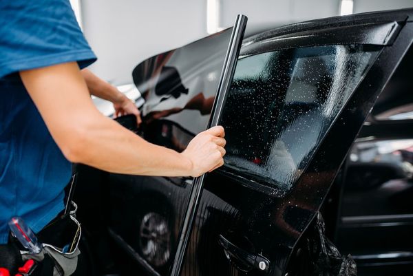 Un homme applique du verre teinté sur la vitre d’une voiture.