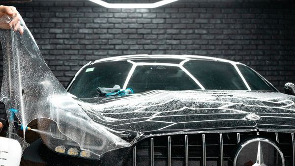 Une personne tient un morceau de plastique au-dessus d’une voiture.