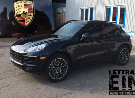 Une Porsche Macan noire est garée devant un immeuble.