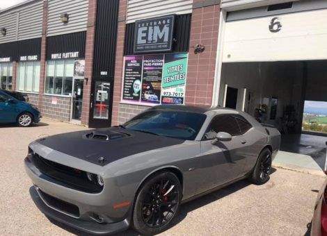Une Dodge Challenger grise est garée devant un immeuble.