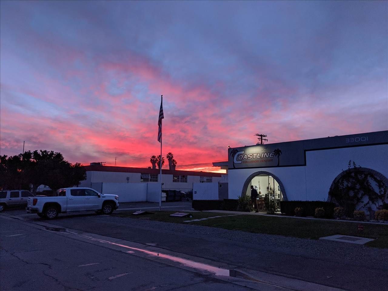Sunset over a building with a flag and a white truck parked on the street.