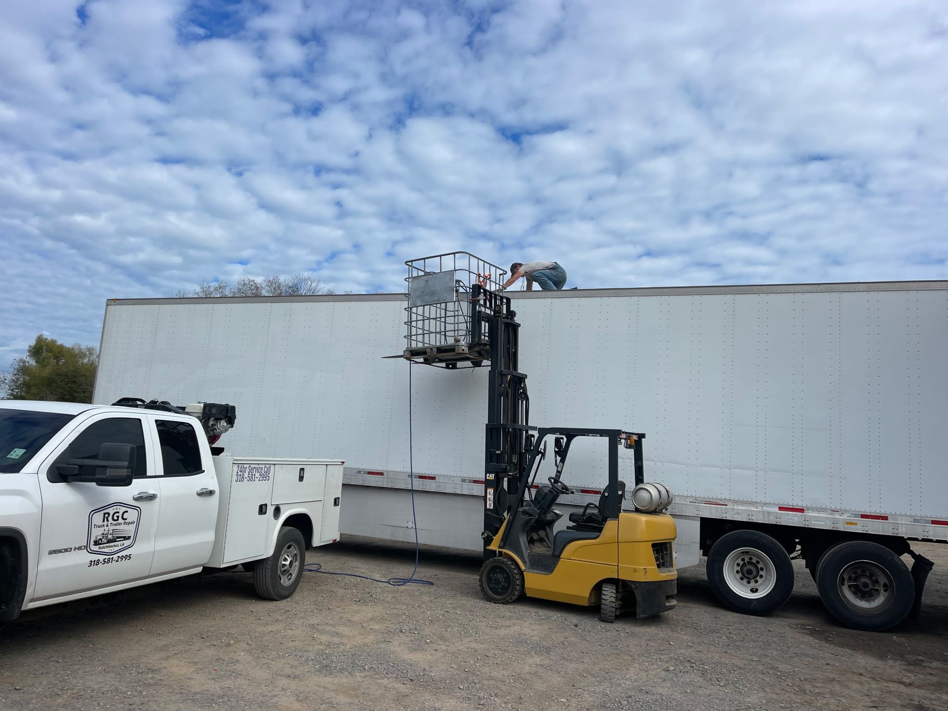 A truck and a forklift are parked next to a large white trailer.