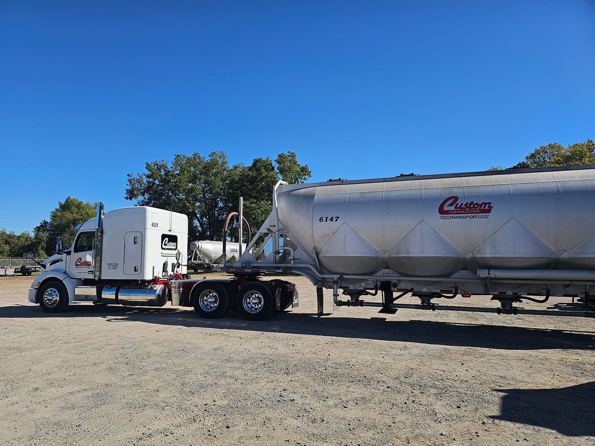 A semi truck with a trailer attached to it is parked in a gravel lot.