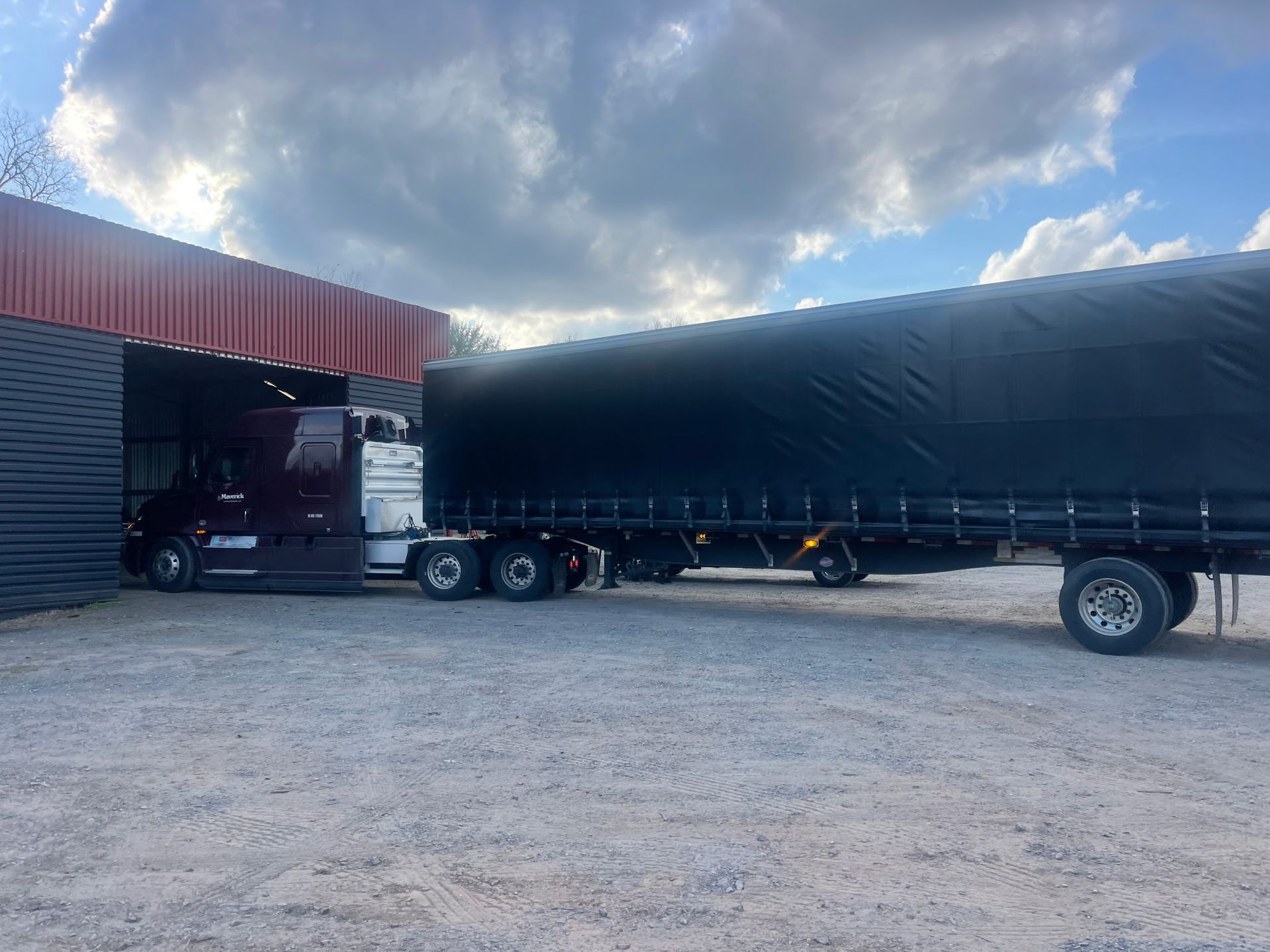 A semi truck with a black tarp on the back is parked in front of a building.