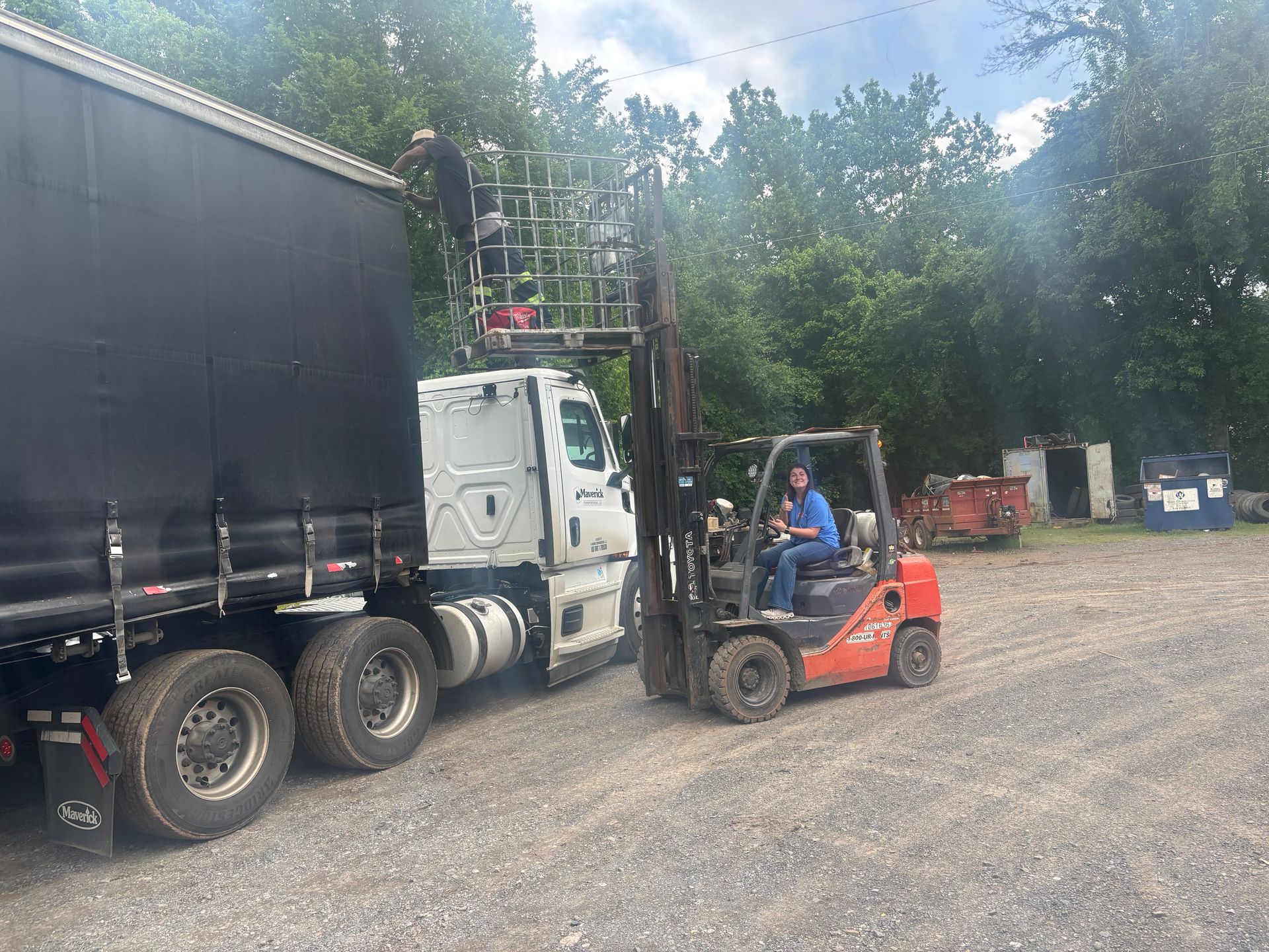 A man is driving a forklift next to a semi truck.