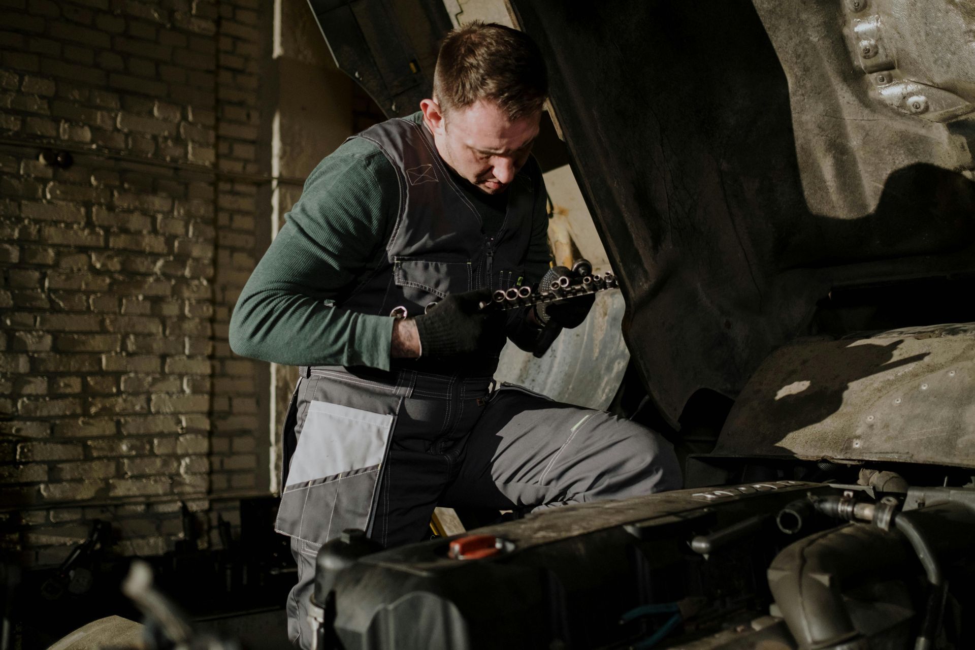 A man is working on a car in a garage with the hood up.
