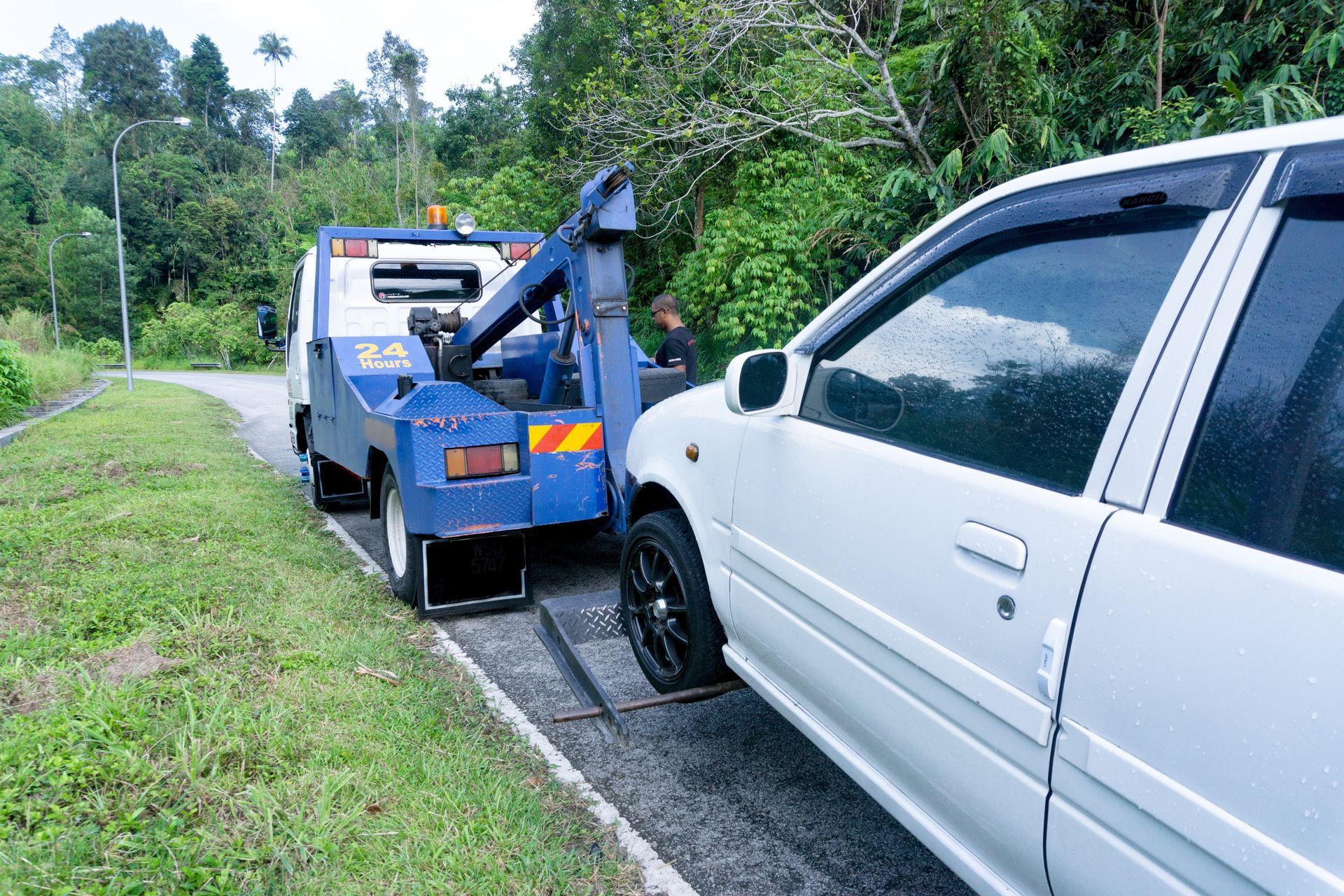 A tow truck is towing a white car on the side of the road.