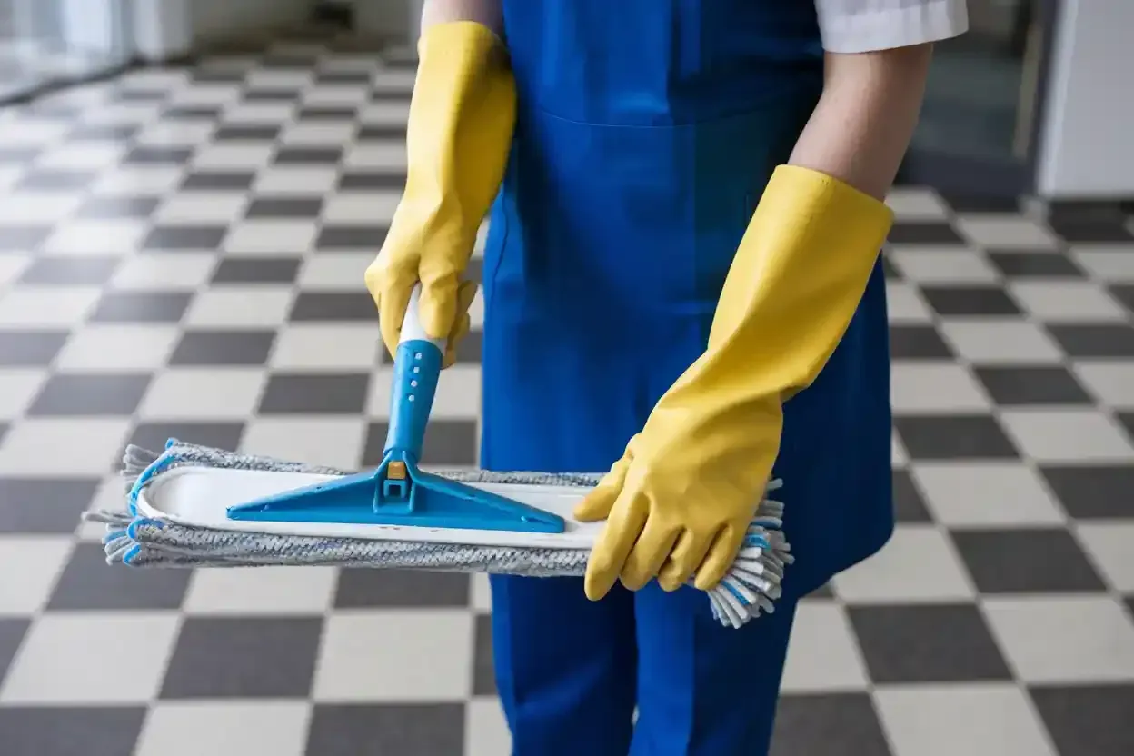 A person wearing yellow gloves is holding a mop and brush.