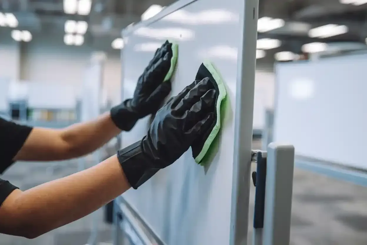 A person wearing black gloves is cleaning a white board with a sponge.