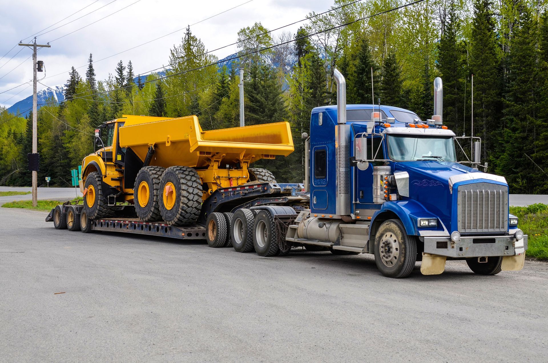A Blue Truck Is Carrying a Yellow Dump Truck on a Trailer — Pearl, MS — Hall’s Towing Service
