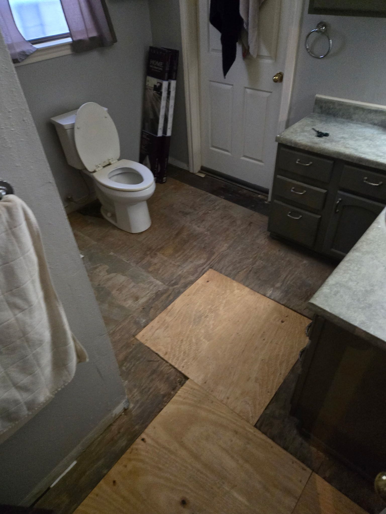 A bathroom with a toilet , sink , and wooden floor.