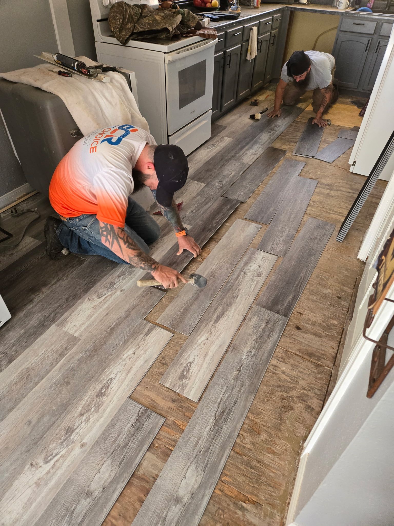 Two men are working on a wooden floor in a kitchen.