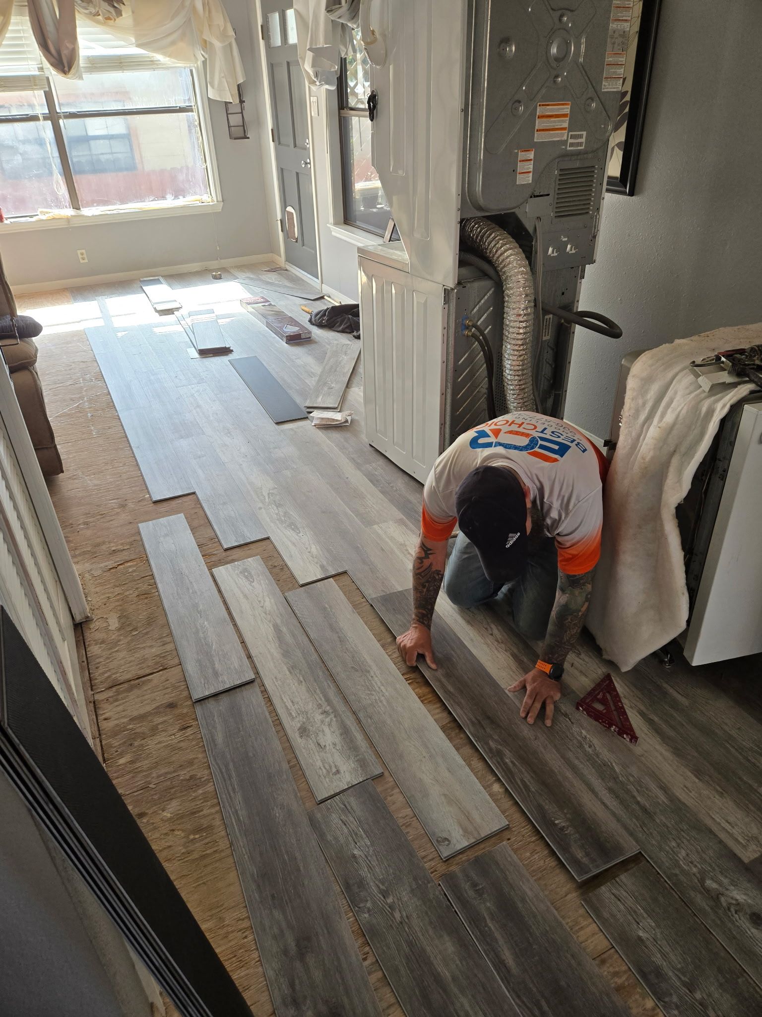 A man is installing hardwood flooring in a living room.
