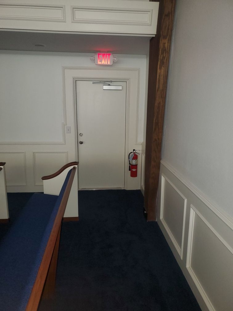 A hallway with a white door and a red exit sign