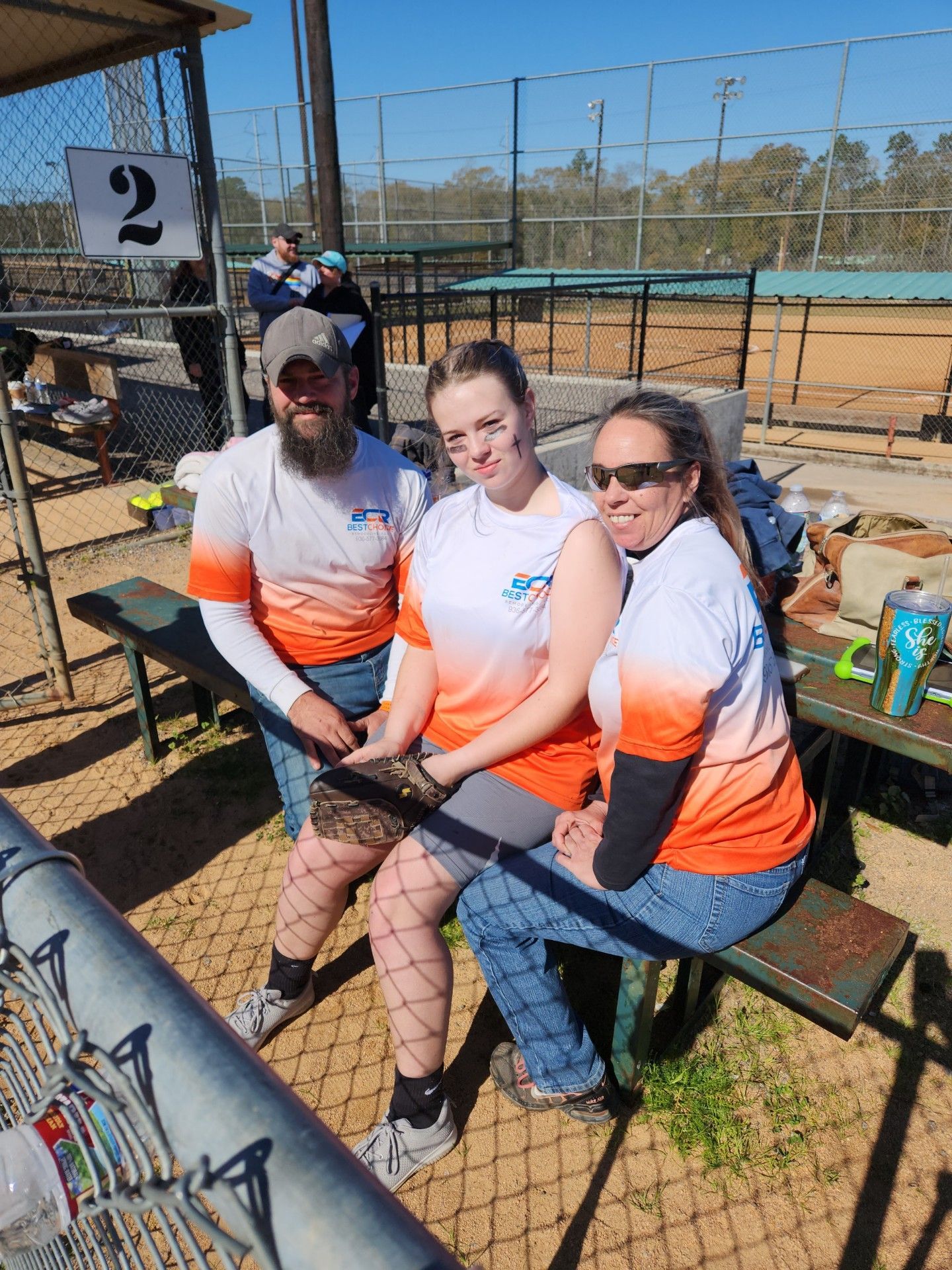 A group of people are sitting on a bench at a baseball field.