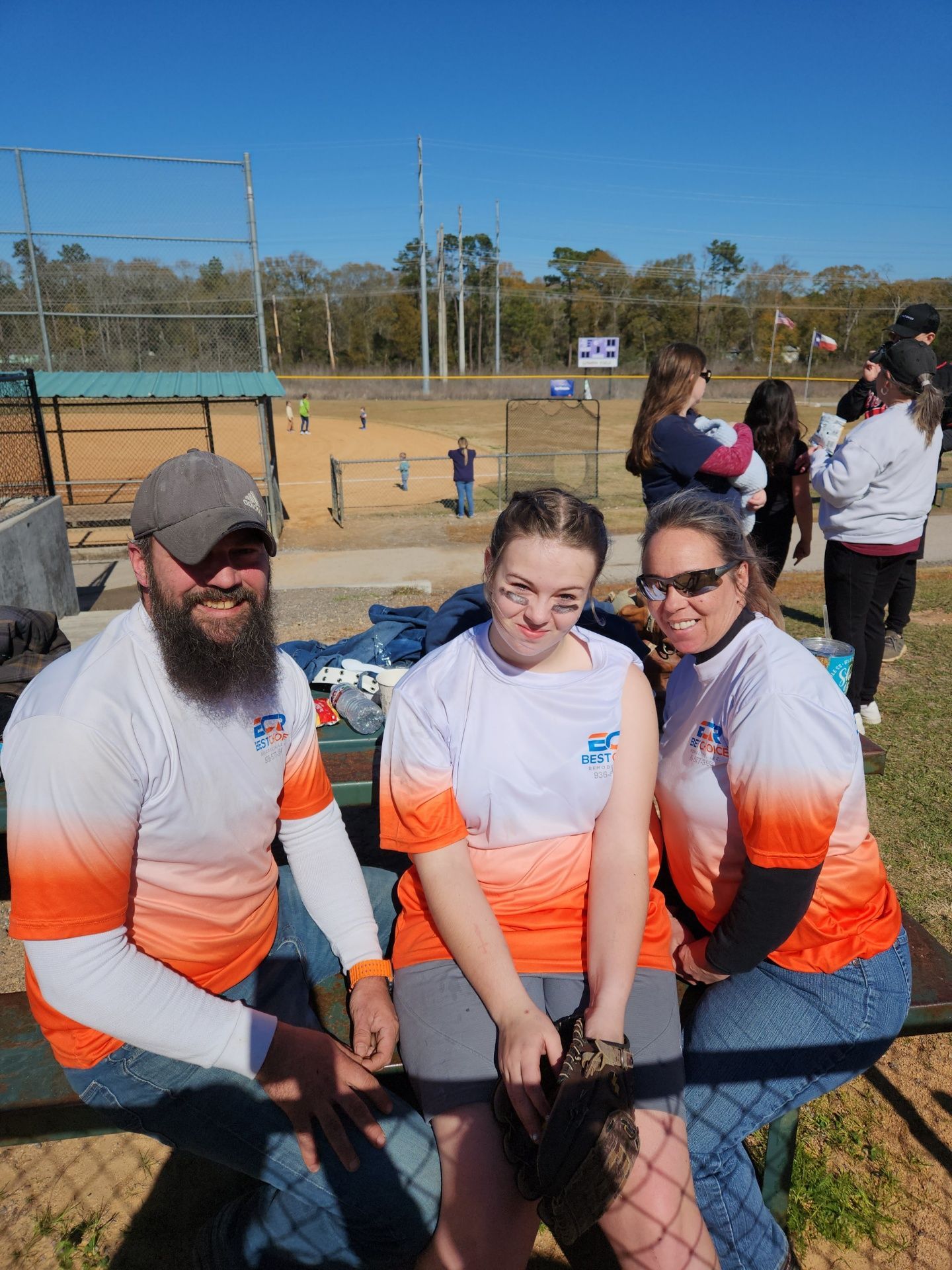 A group of people are sitting on a bench at a baseball field.