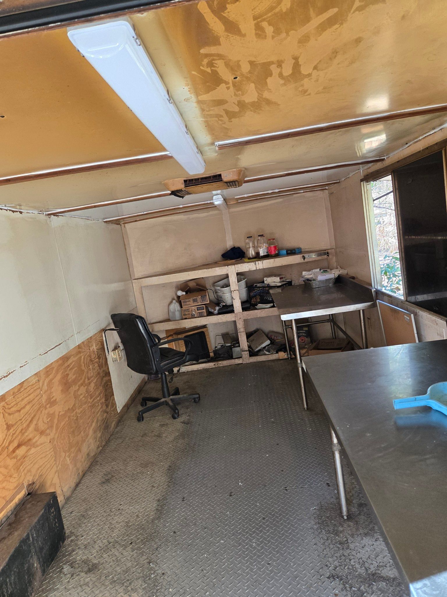 A room with a desk , chair , shelves and a window.