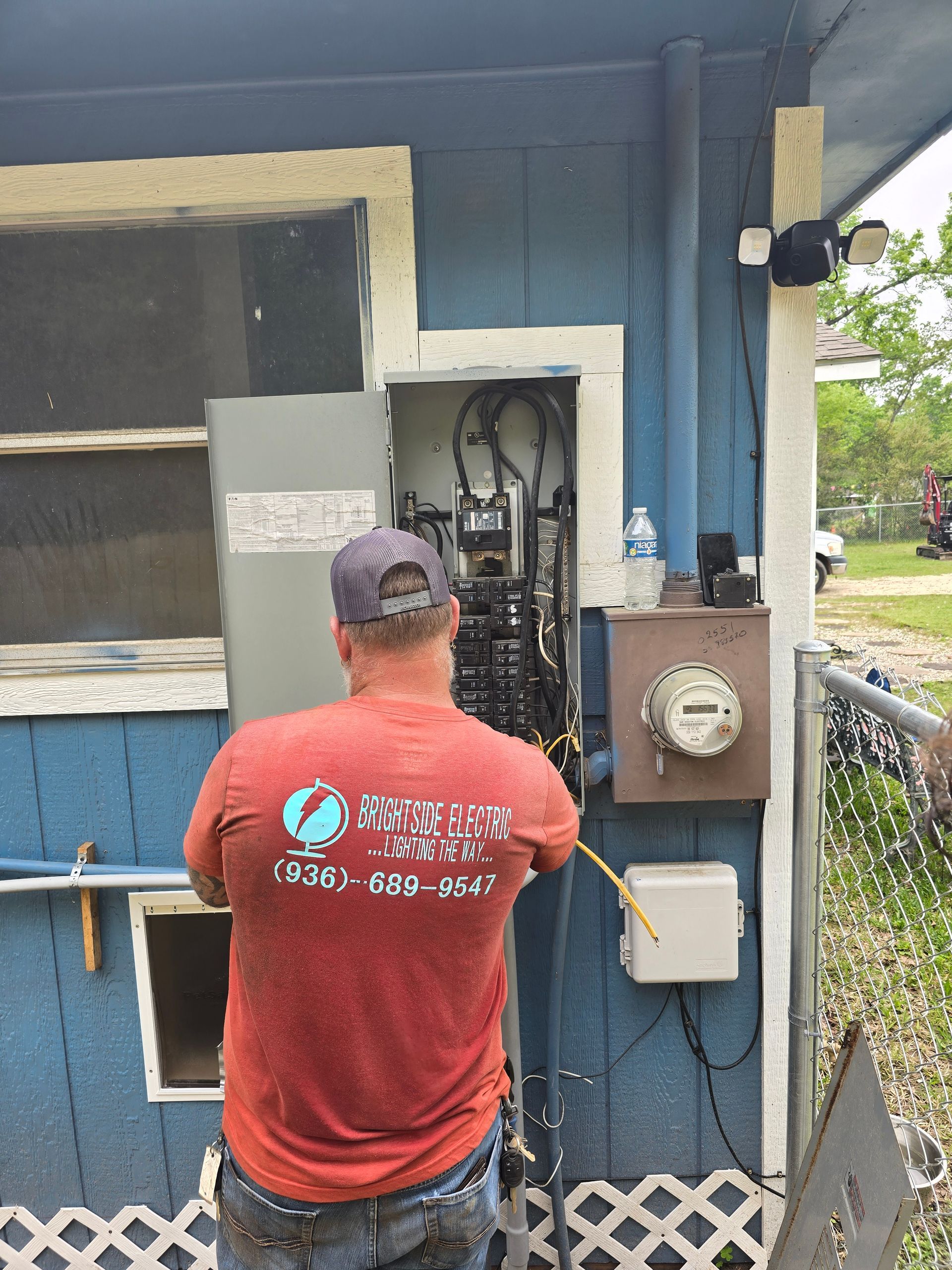 A man in a red shirt is working on an electrical box.