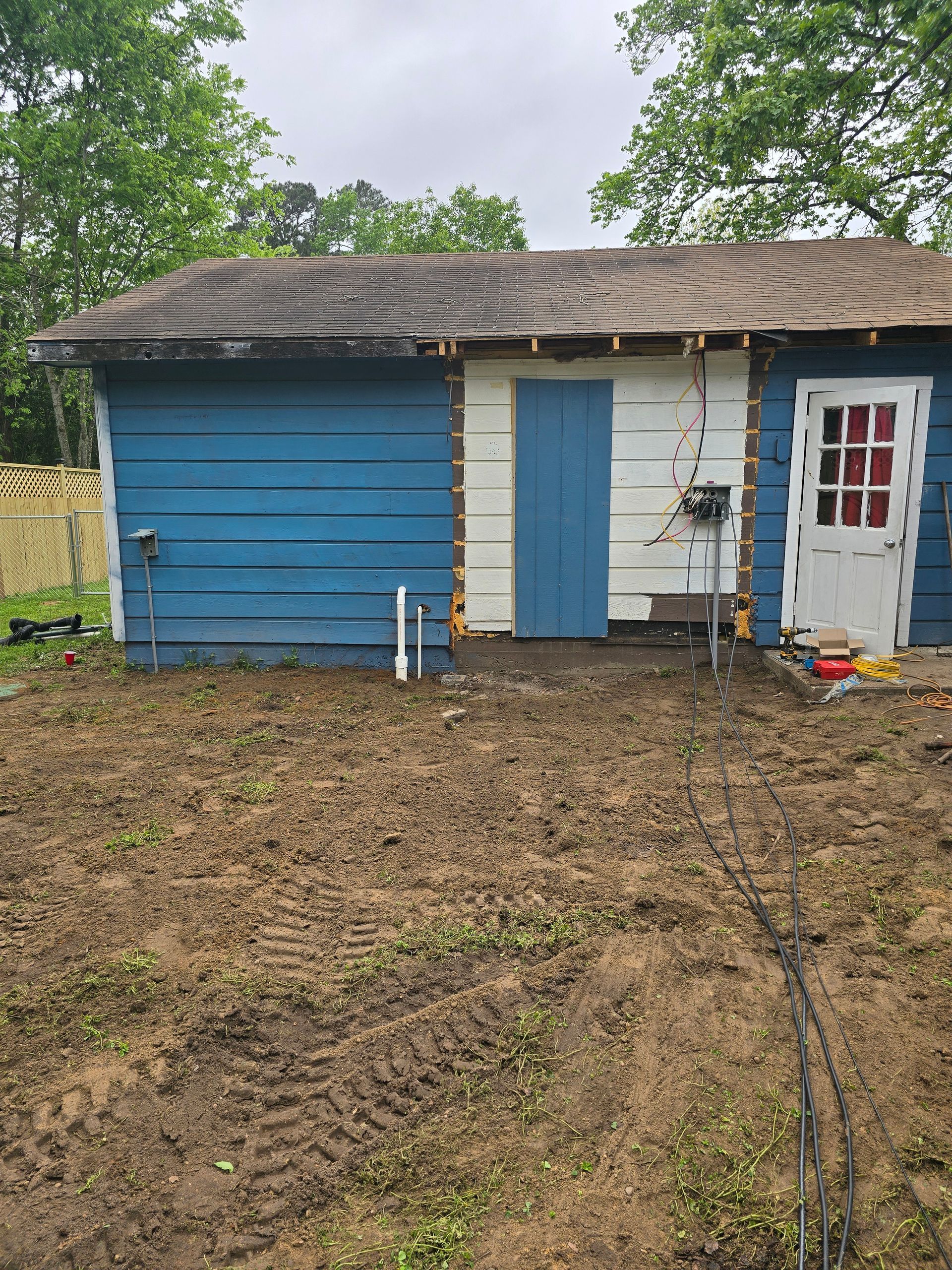 A blue house with a white door is sitting in the middle of a dirt field.