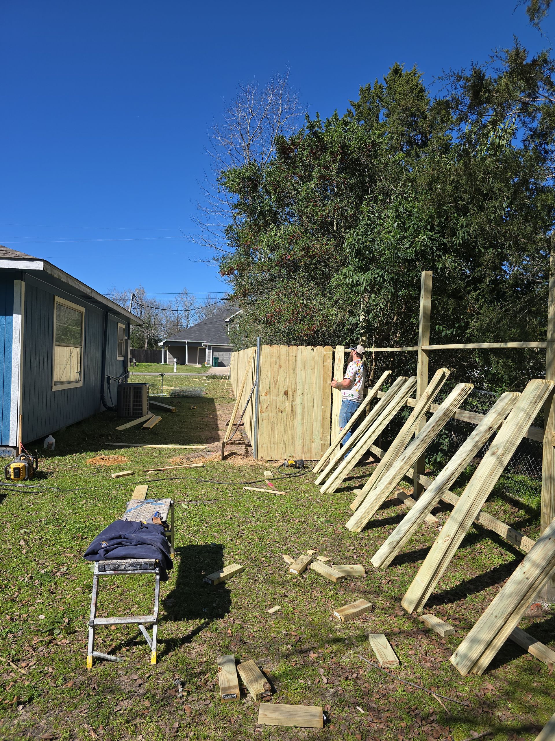 A man is working on a wooden fence in the backyard of a house.