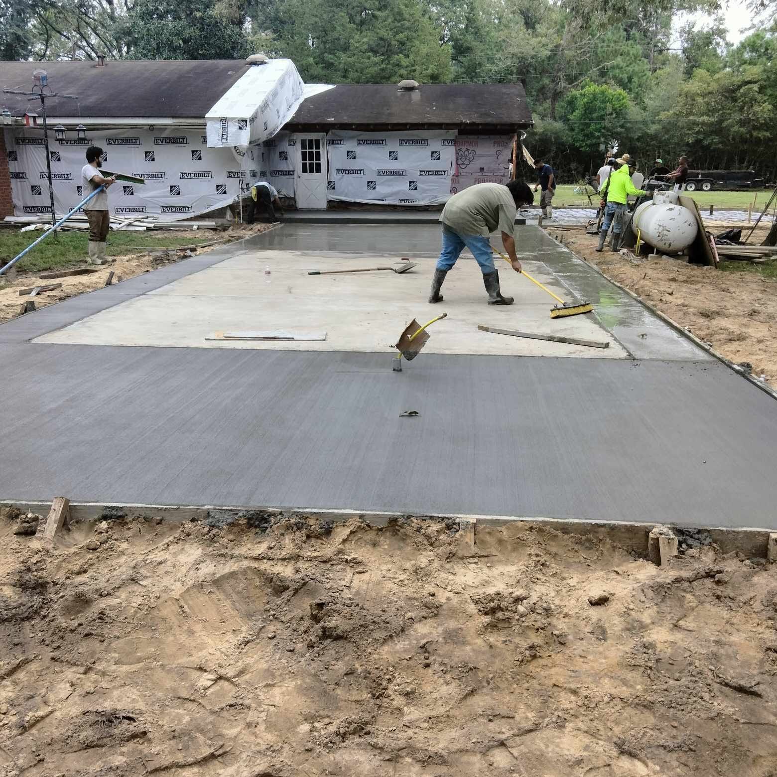 A man is working on a concrete driveway in front of a house.