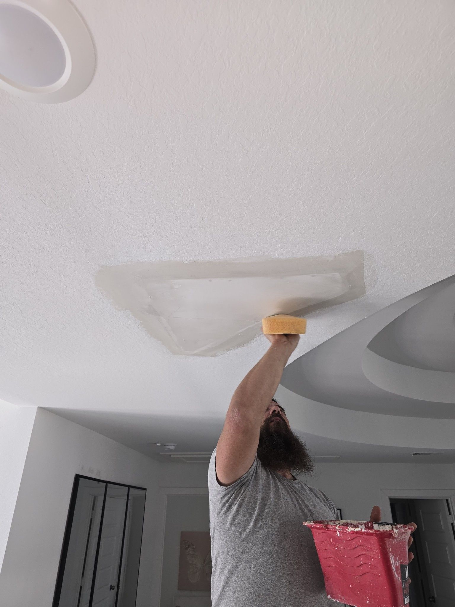 A man is painting a ceiling with a sponge.