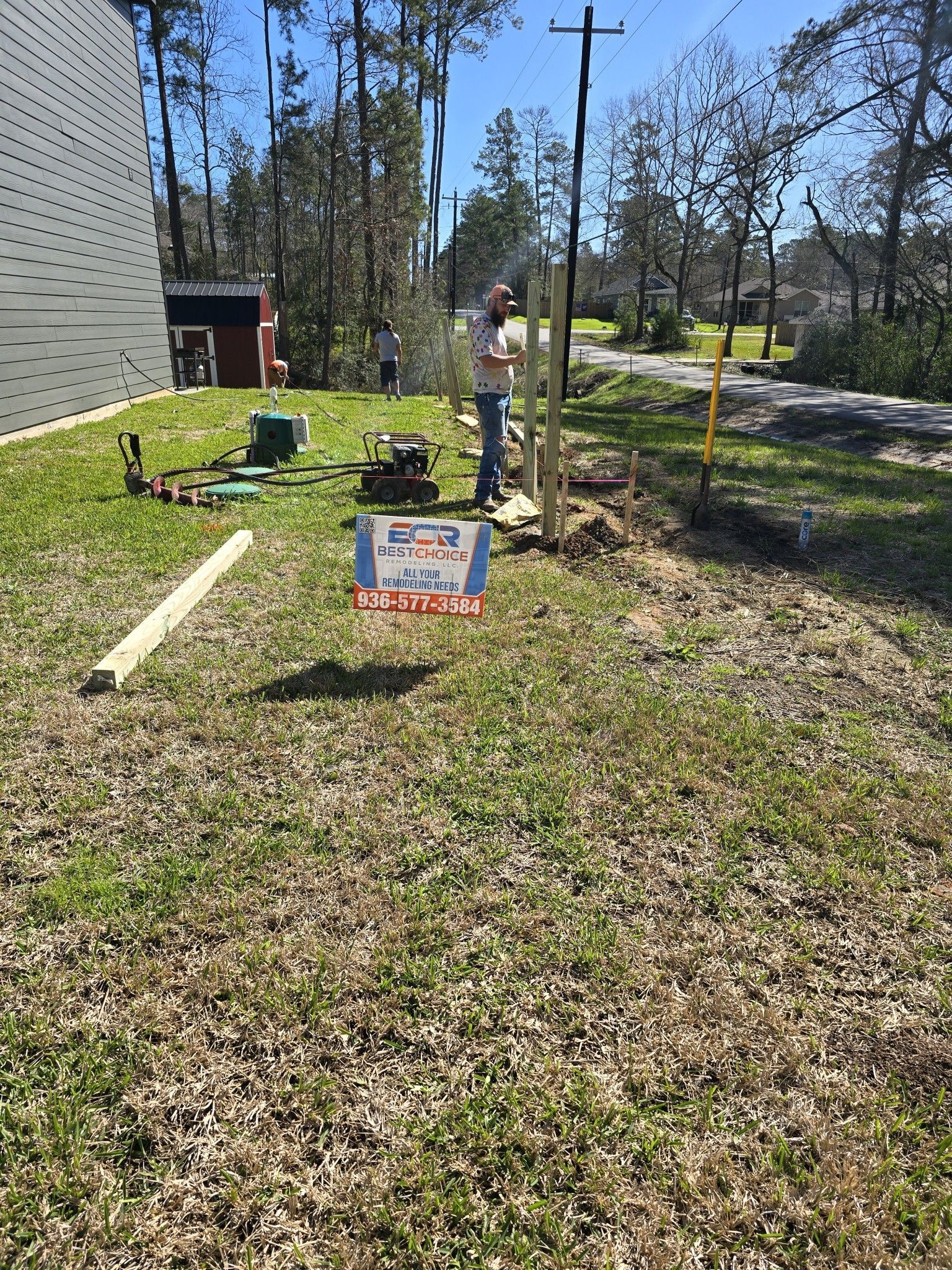 A man is working on a fence in a grassy field.