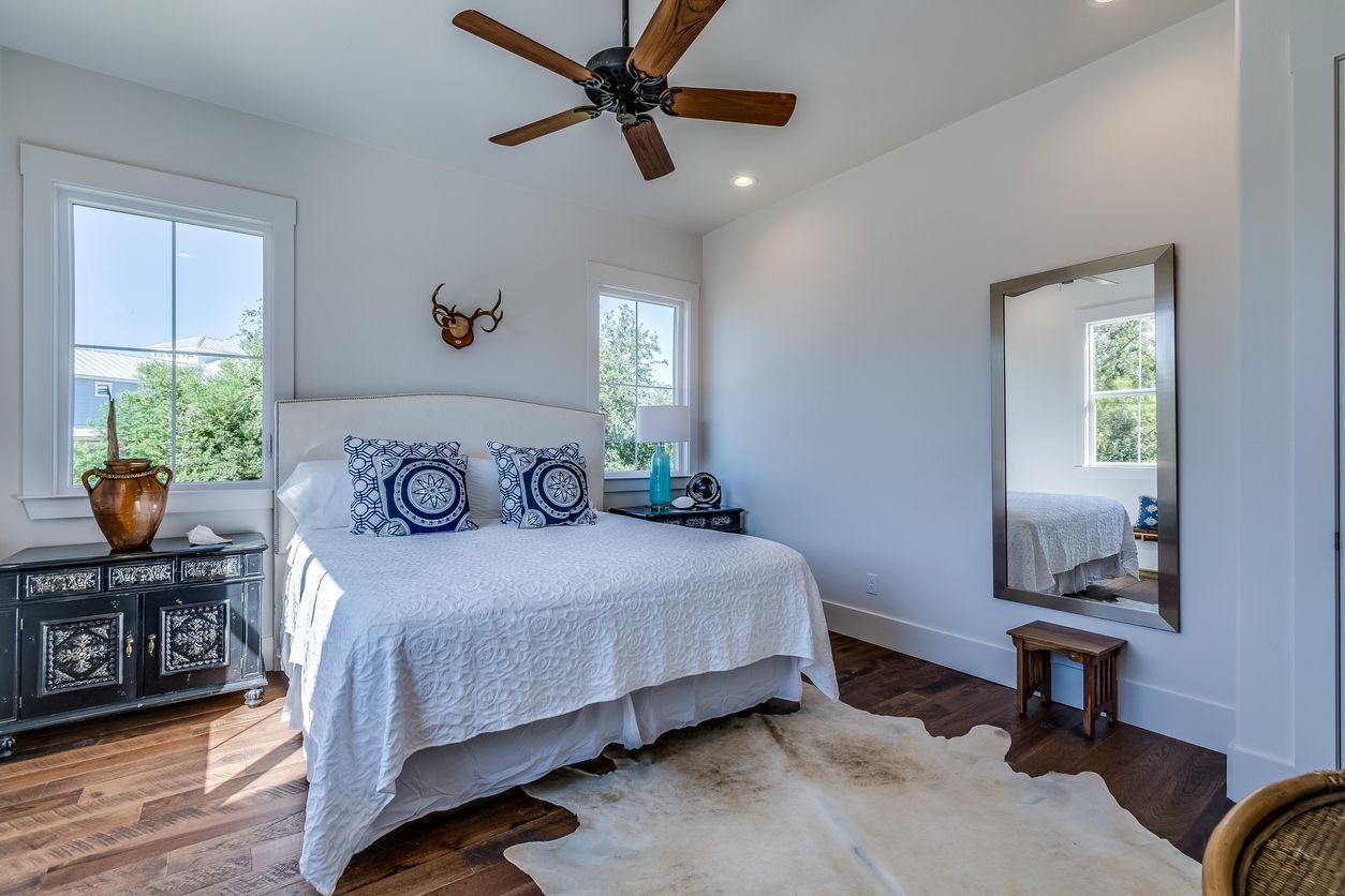 A bedroom with a large bed , a ceiling fan , a mirror and a cowhide rug.