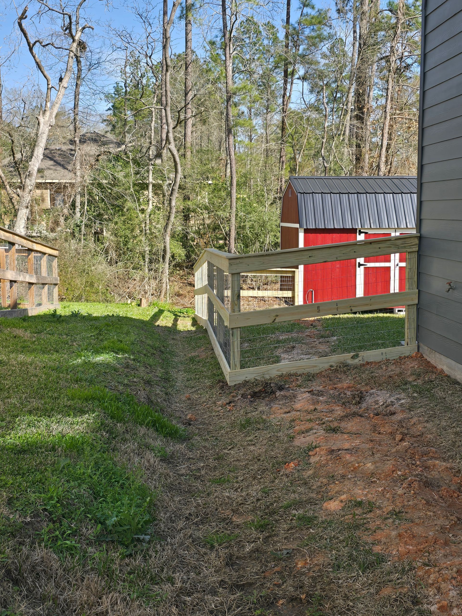 A wooden fence is in the backyard of a house next to a red barn.