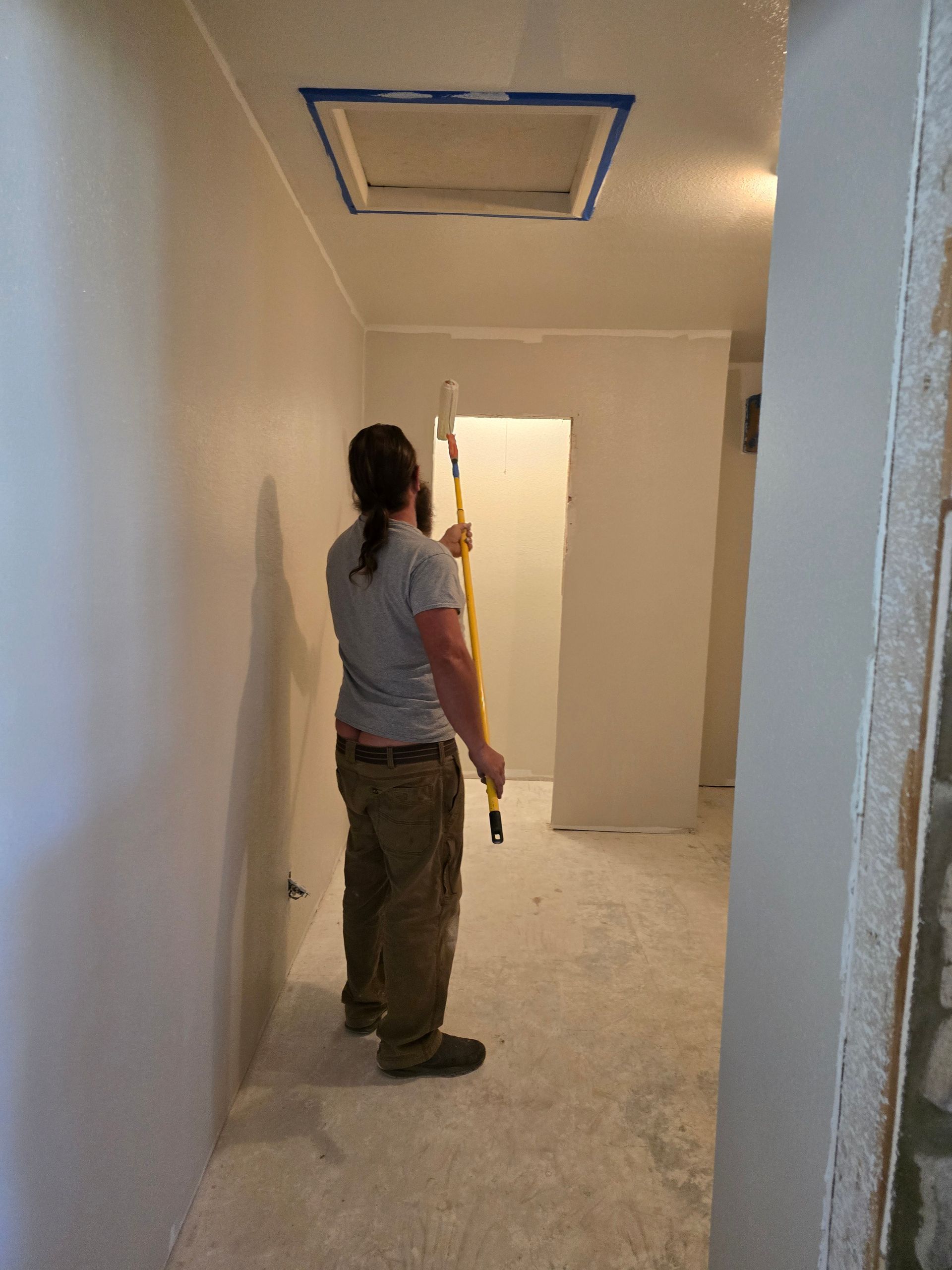 A man is standing in a hallway holding a paint roller.