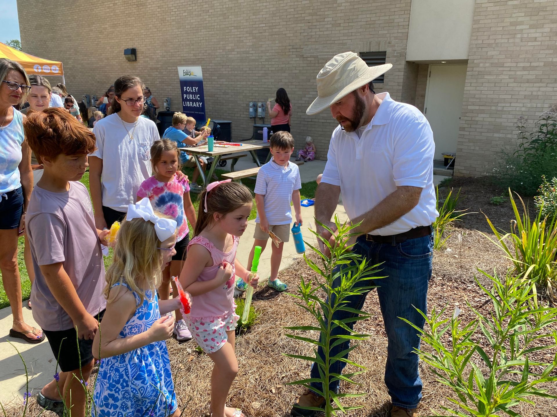 Children examine a native milkweed plant with infant Monarch butterfly caterpillars on the leaves.