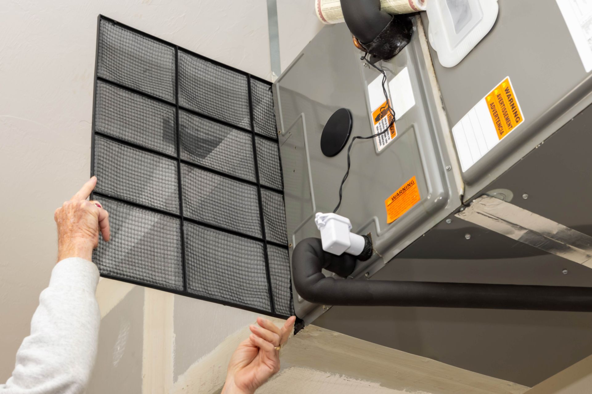Person replacing an air filter in an HVAC system; hands holding the filter and the unit's door.