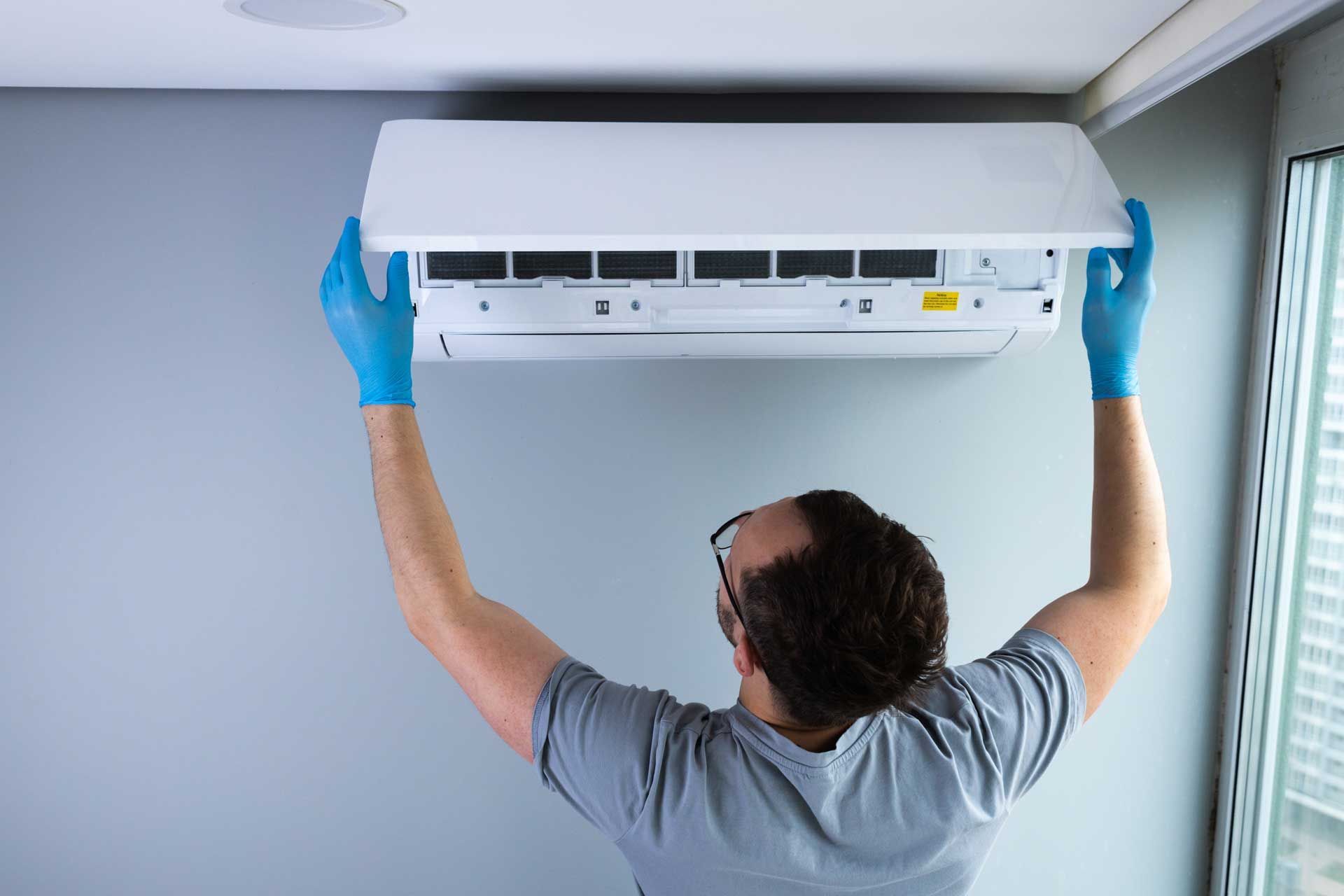 Person in blue gloves servicing a white wall-mounted air conditioner.