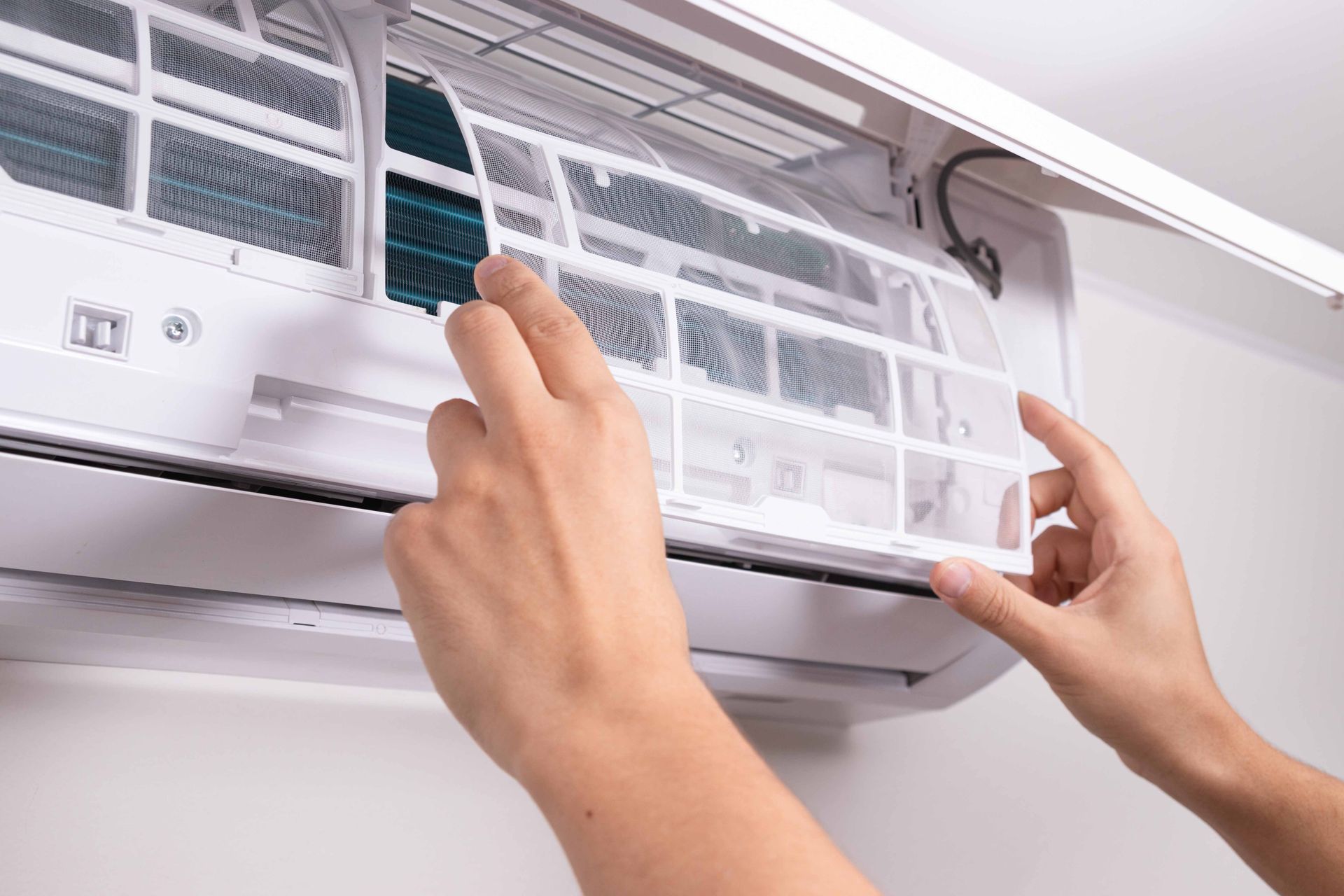 Hands removing air filter from a wall-mounted air conditioning unit.