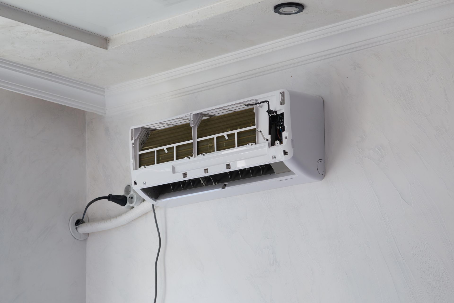 White air conditioning unit mounted on a white wall, partially disassembled.