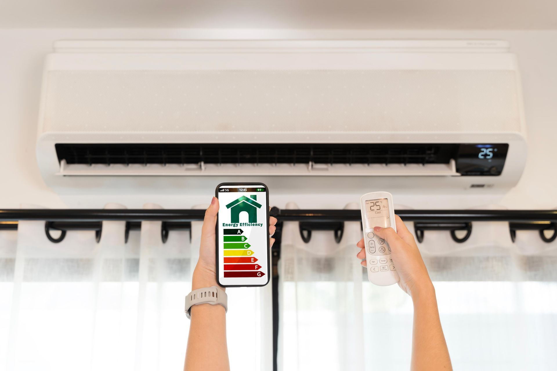 Person operating air conditioner with smartphone showing energy efficiency, and remote control.