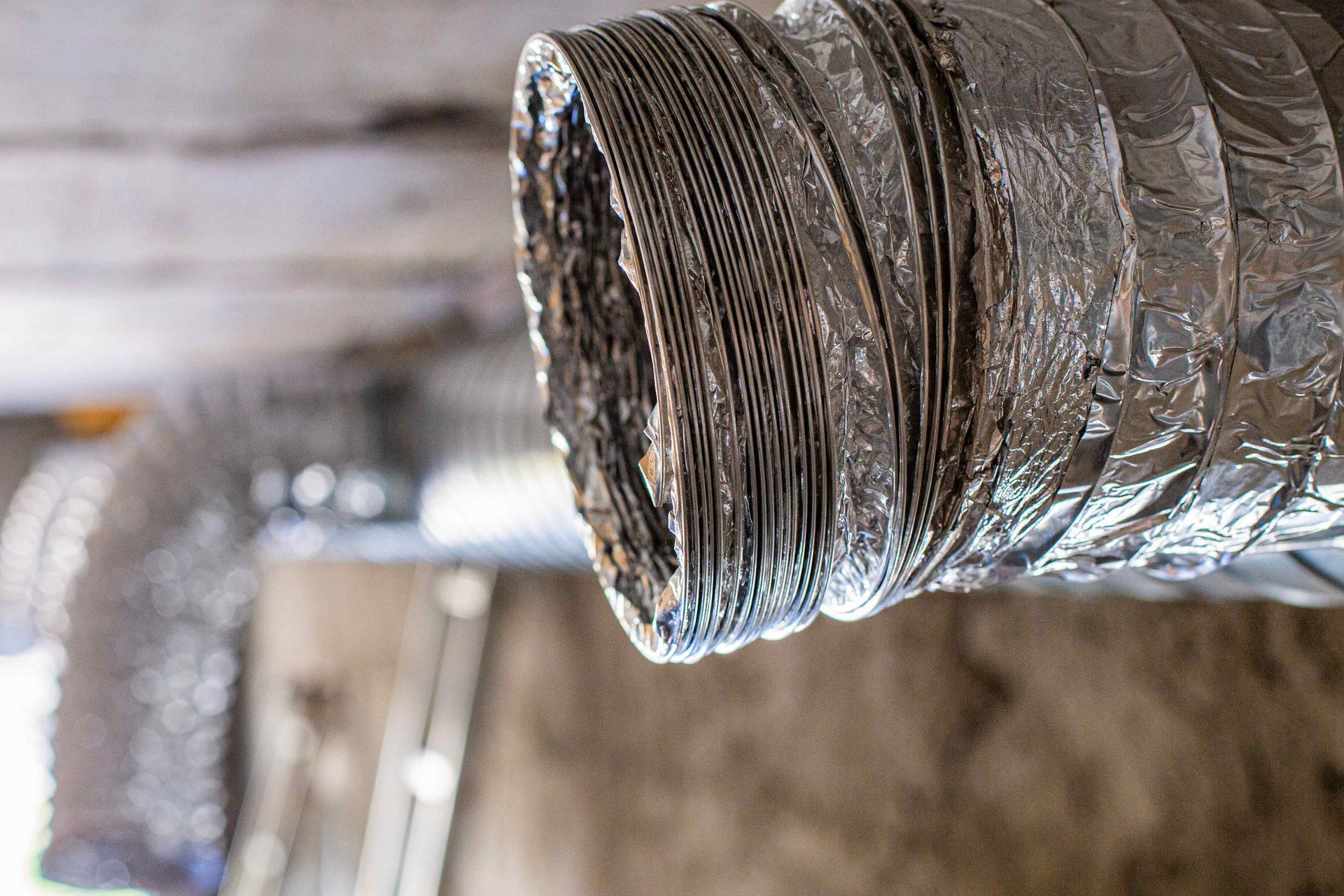 Flexible metallic ductwork, partially unraveled, hangs from a ceiling.