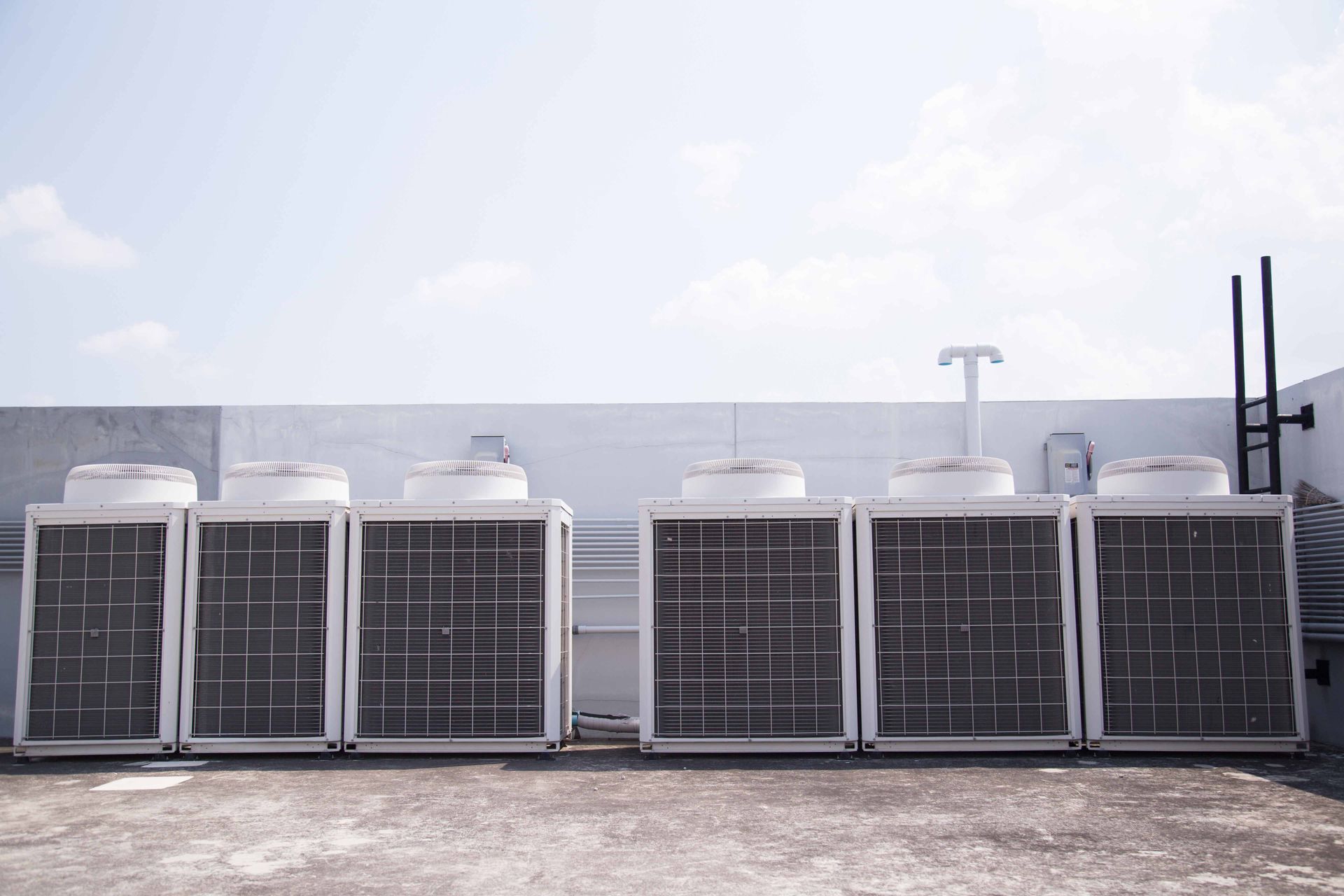 Six air conditioning units on a rooftop, white and gray against a blue sky.