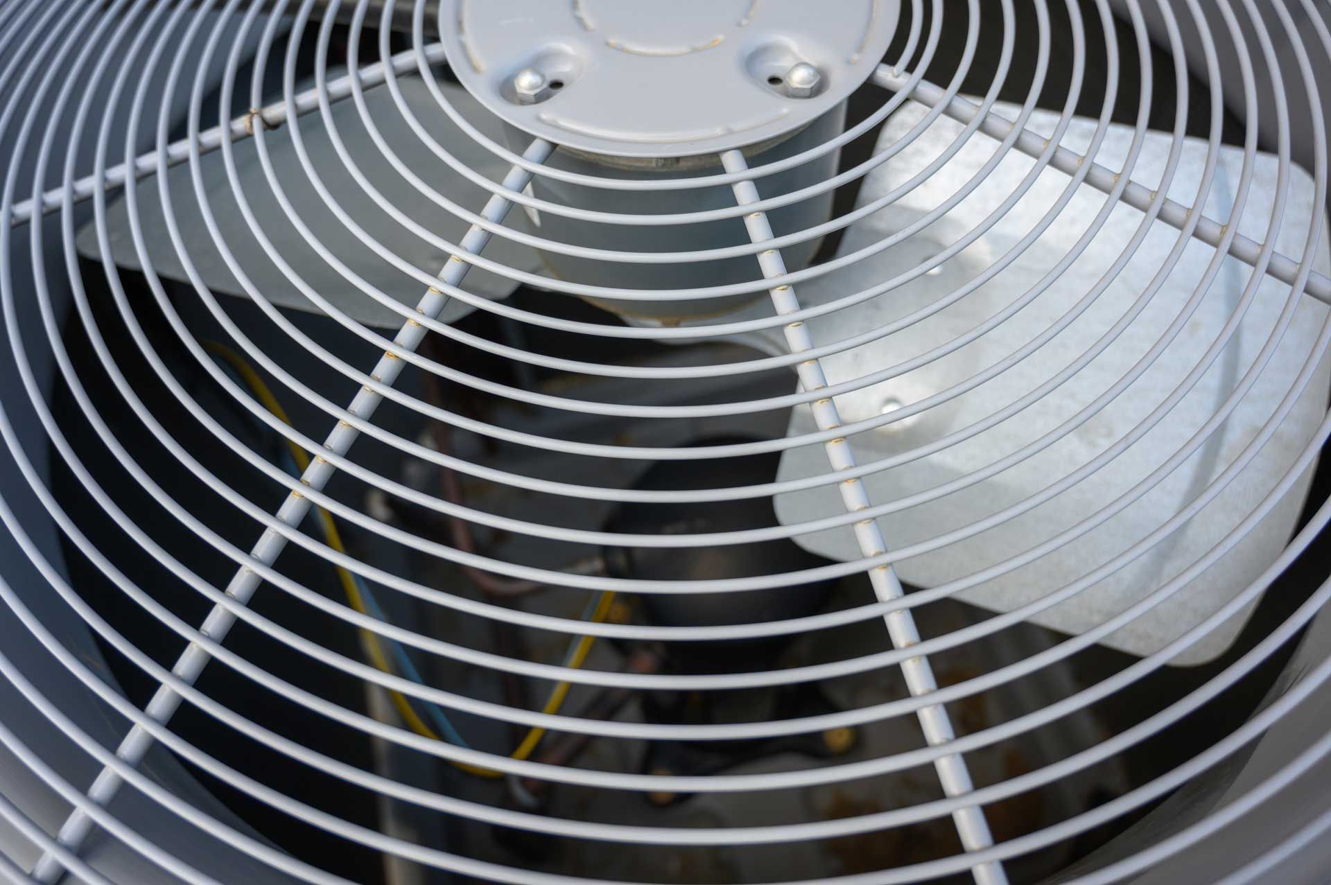 Close-up view of an air conditioning unit fan with a protective metal grill.