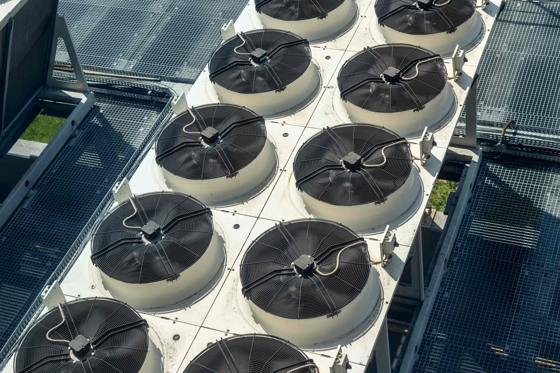 Rows of industrial cooling tower fans on a rooftop, black blades, white supports.