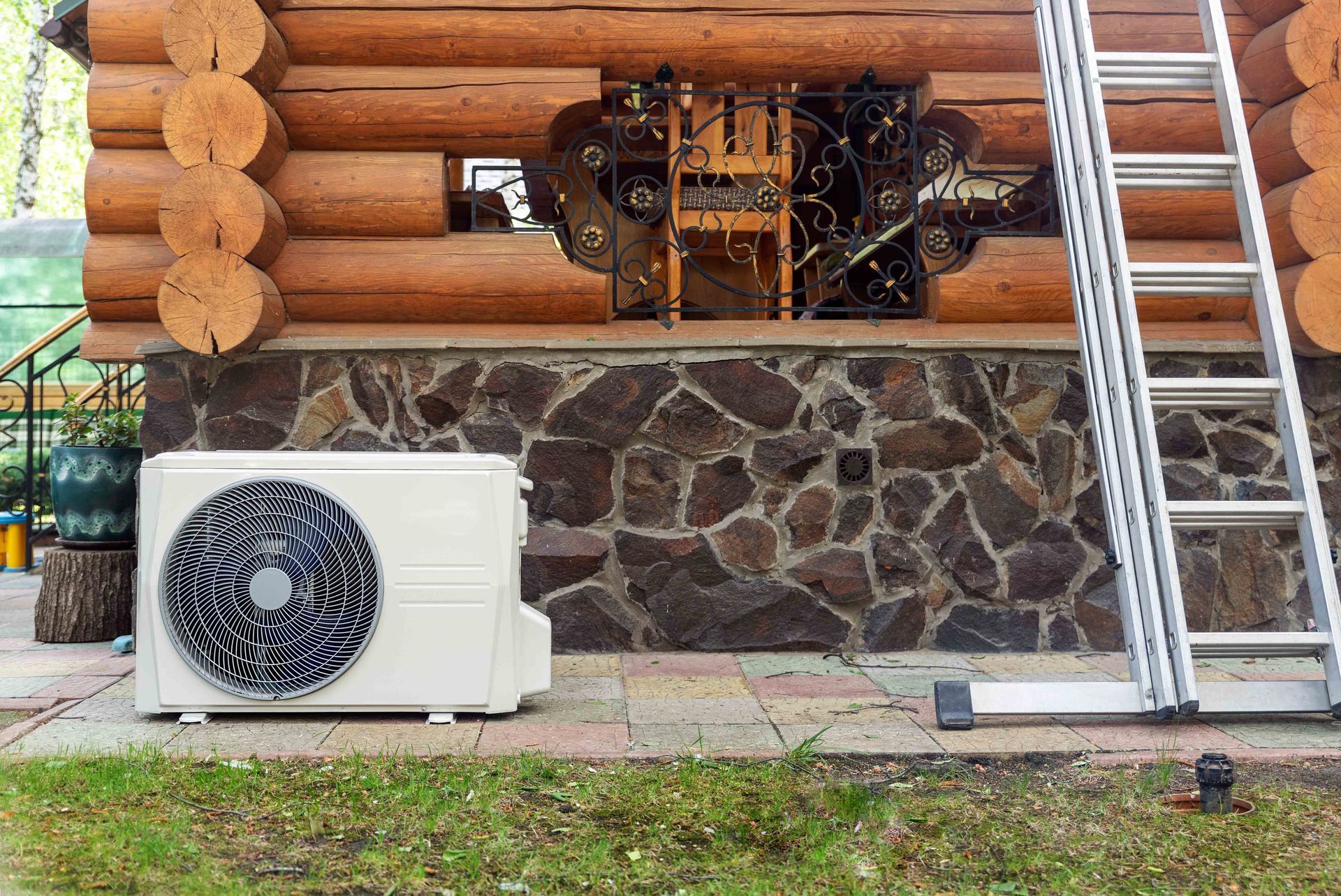 Air conditioner unit next to a stone wall and log cabin with a ladder leaning against it.