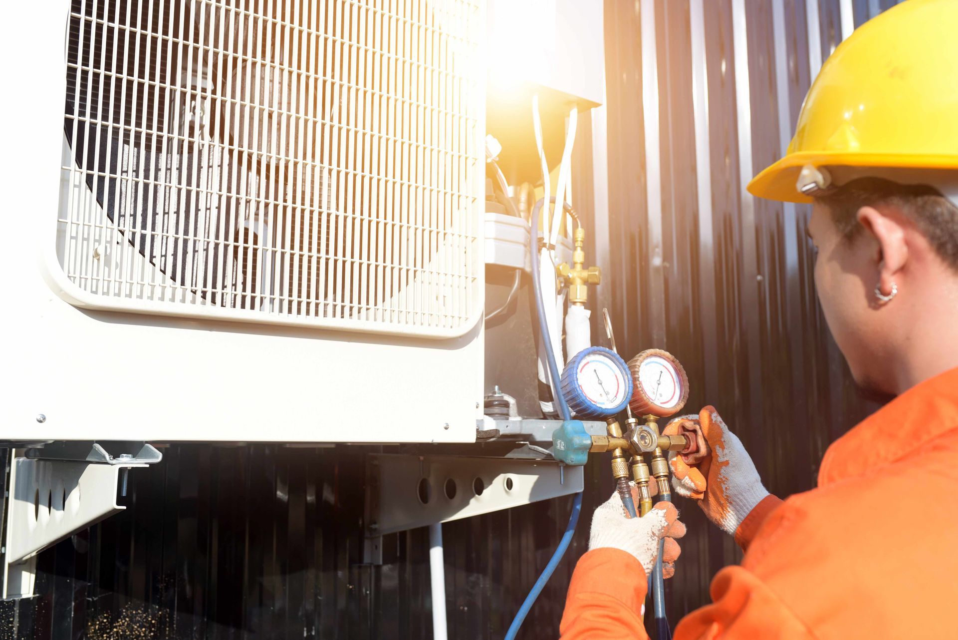 HVAC technician in an orange jumpsuit and hardhat working on an air conditioning unit.