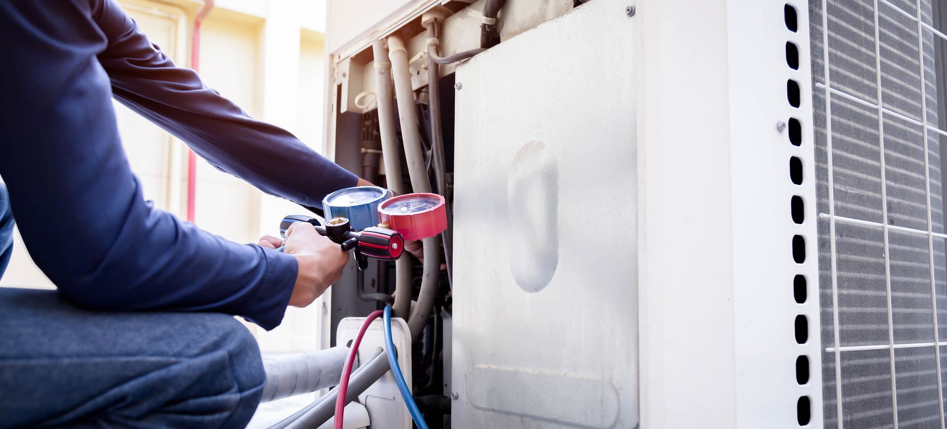 A technician using gauges to service an outdoor air conditioning unit.