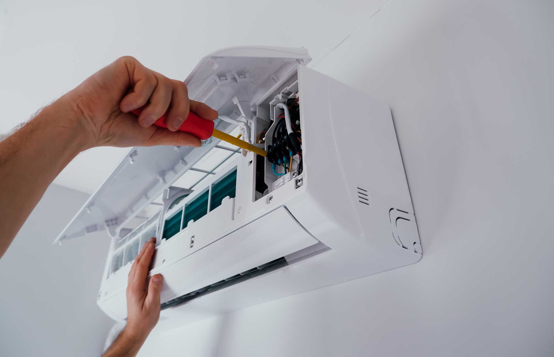 Person repairs white wall-mounted air conditioner with a screwdriver.