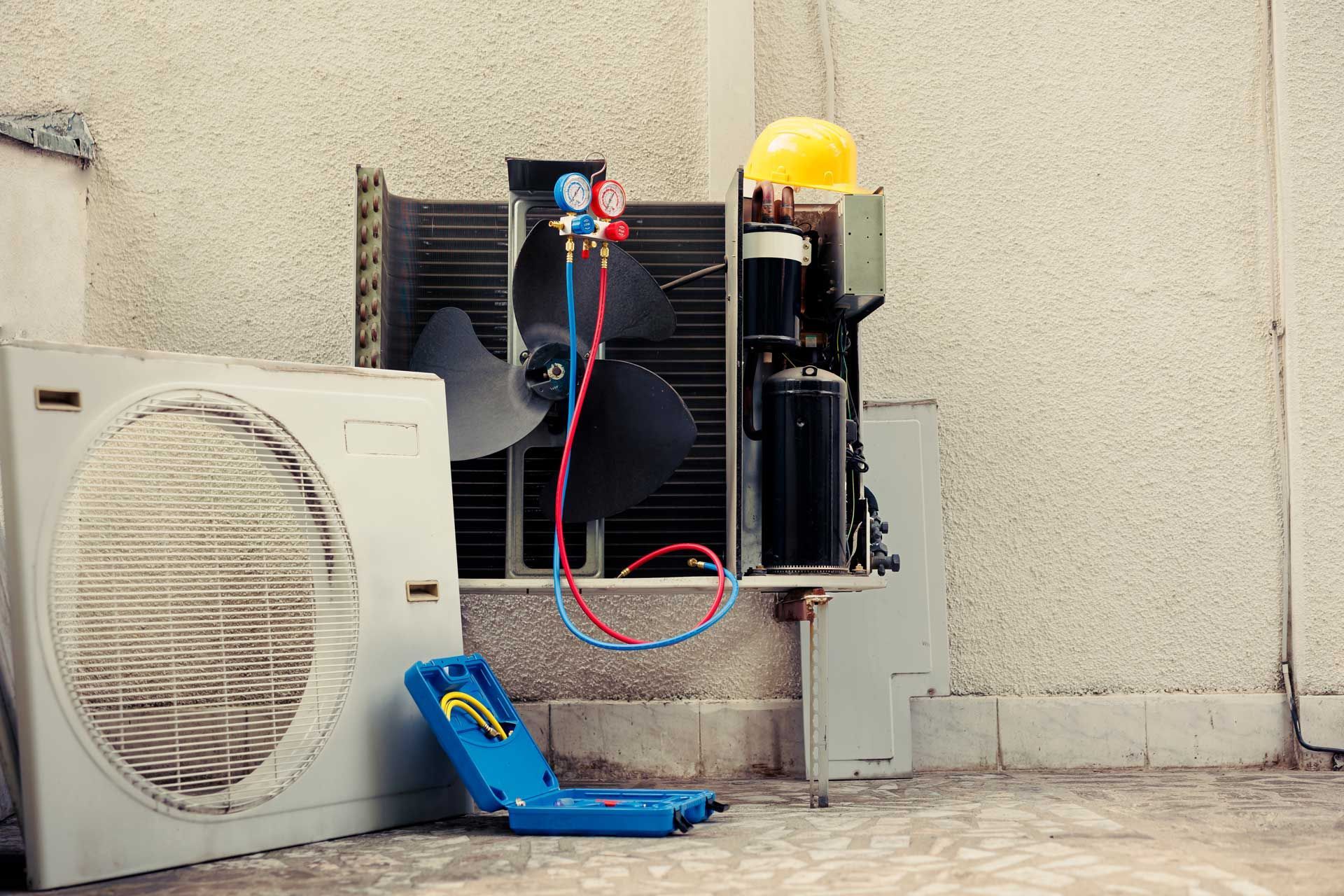 HVAC technician repairing an outdoor air conditioning unit with gauges, tools, and a fan.