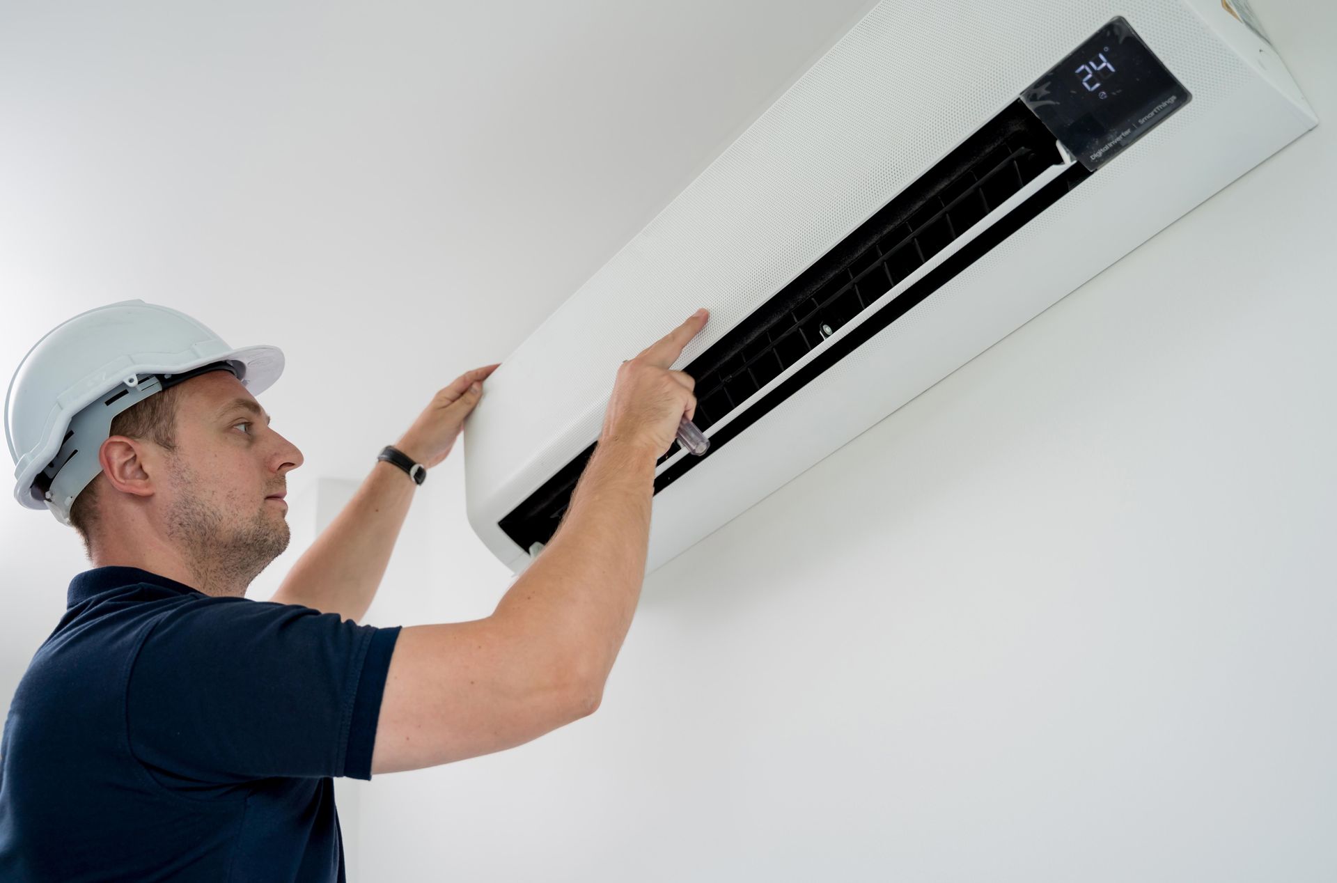 Man in hard hat installing an air conditioner on a white wall.
