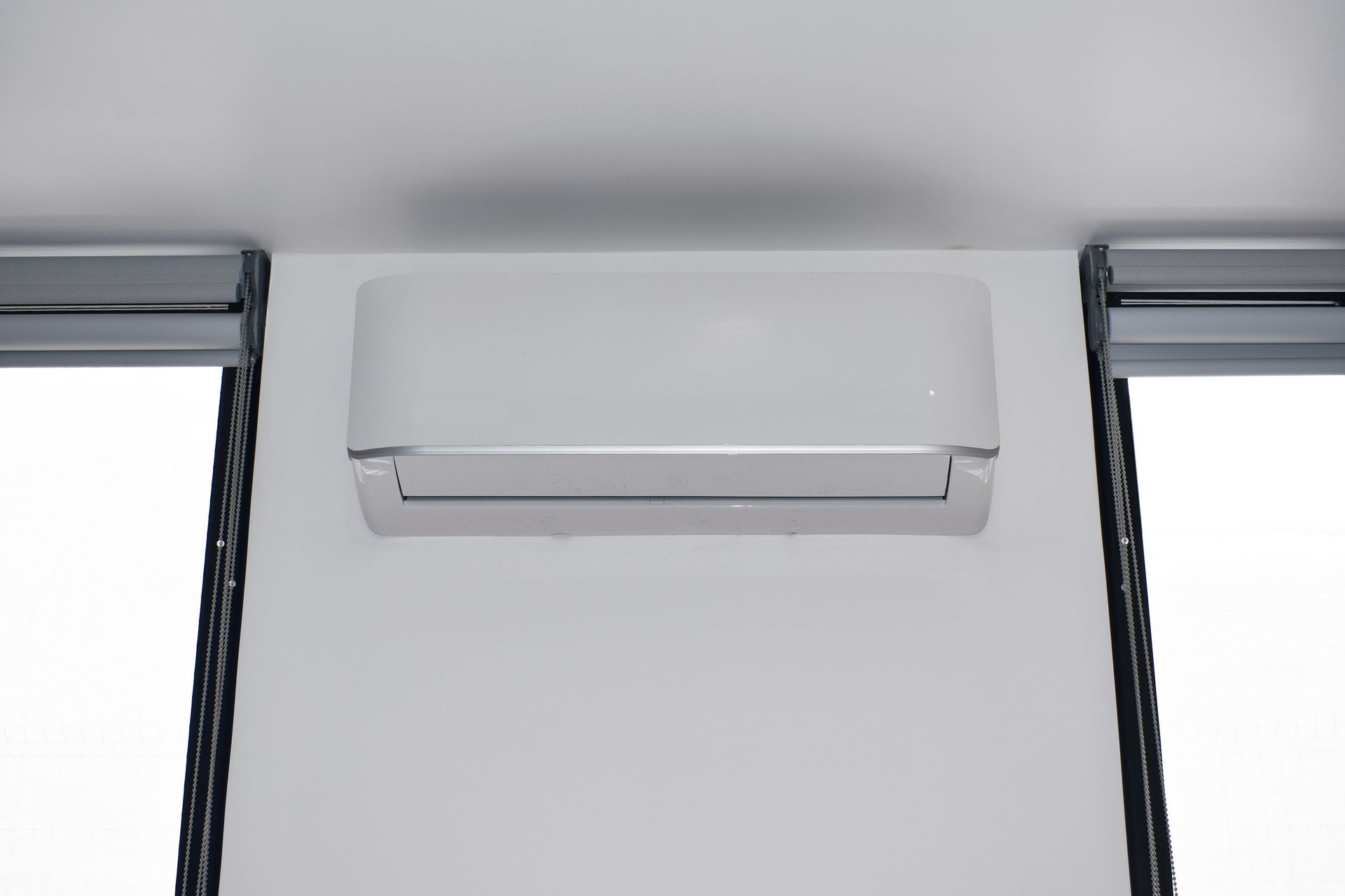 White air conditioning unit mounted on a white wall between two window panels.