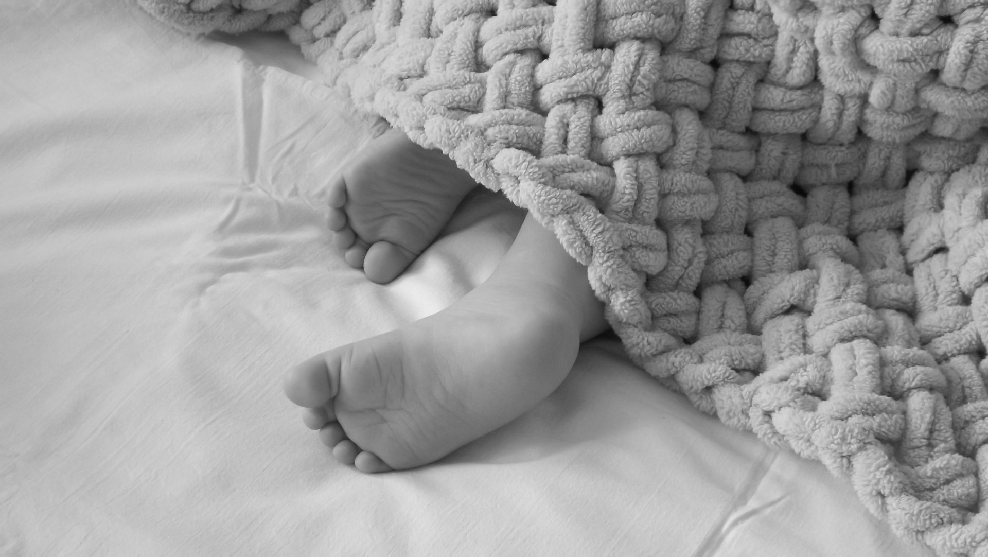 Black and white photo of a child's feet under a knitted blanket